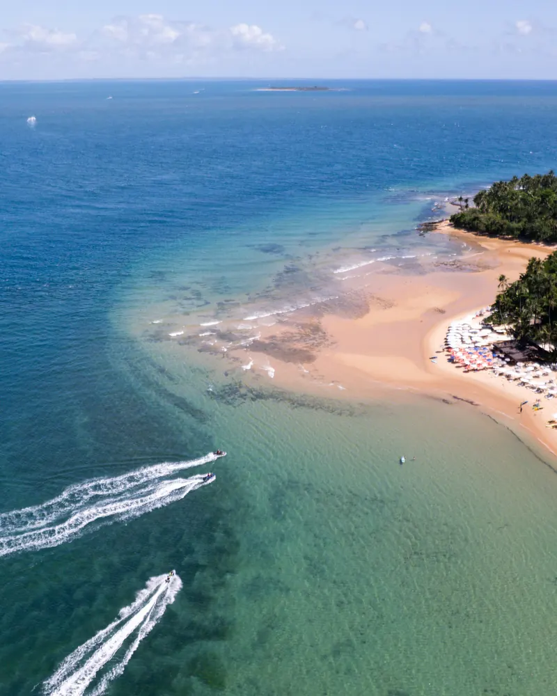 A sandy point with light-green sea and speedboats, seen from above