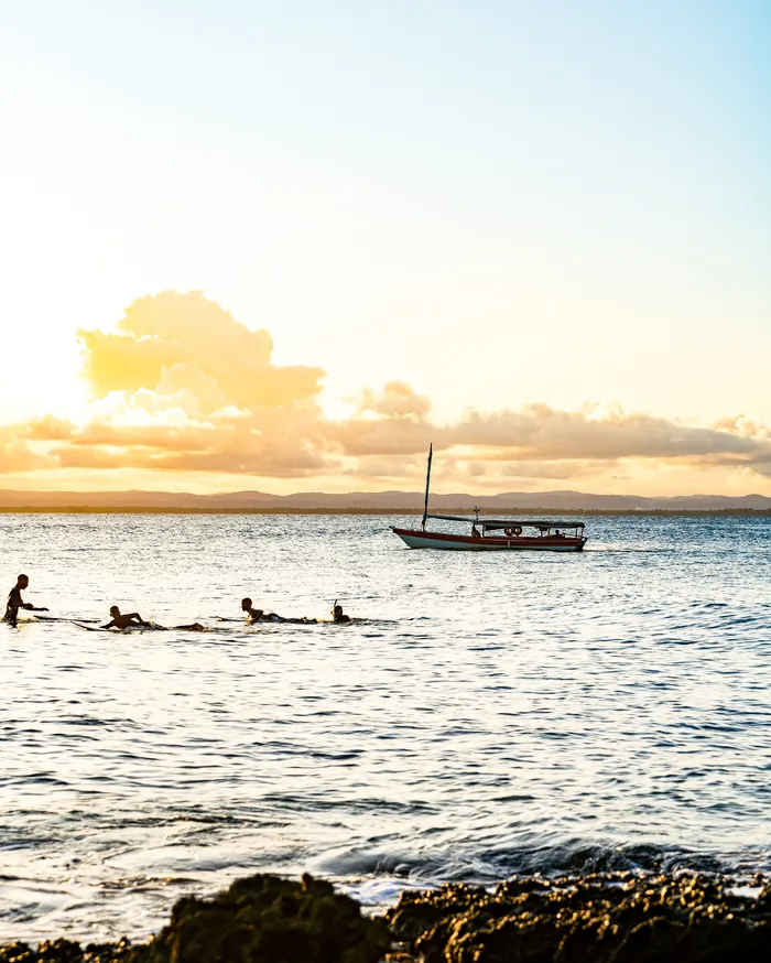 Swimmers and a boat at sunset, with reefs in the foreground